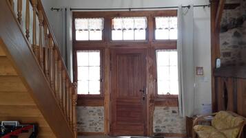 Un escalier en bois avec une rampe, une grande porte en bois dotée de panneaux de verre et un mur en pierre.