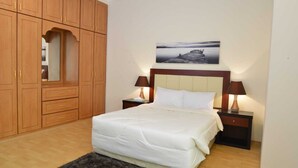 A bedroom with a bed, wooden wardrobe, nightstands, and a painting on the wall. - Near Juffair Oasis Mall / Tow Bedroom Apartment (Jaffer)