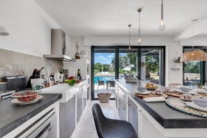 A modern kitchen with a central island, a dining area with a view of a pool, and a large window. - Villa Tartaruga Luxury With Pool (Carovigno)