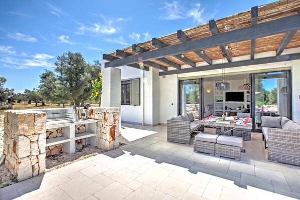 Un área de estar exterior moderna con una parrilla de piedra, asientos y una pérgola.