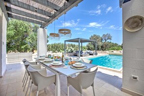 An outdoor dining area with a pool, white chairs, and a covered seating area. - Villa Tartaruga Luxury With Pool (Carovigno)