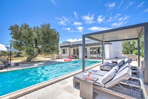 Un área de piscina con sillas de descanso, un comedor y una zona de estar techada.