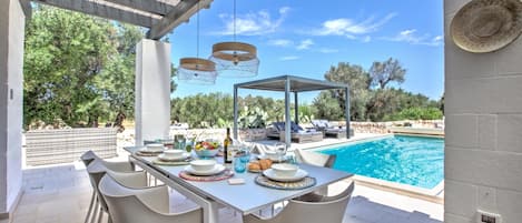 Un espace extérieur aménagé pour les repas, avec une piscine, des chaises blanches et un coin salon abrité.