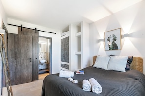 A modern hotel room with a large bed, a wardrobe, a bathroom with a mirror, and a wall-mounted artwork.