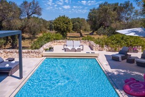 A swimming pool with lounge chairs and a stone wall.