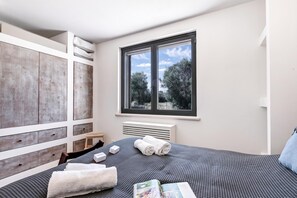 A bedroom with a large window, a bed with towels, a wooden wardrobe, and a radiator. - Villa Tartaruga Luxury With Pool (Carovigno)