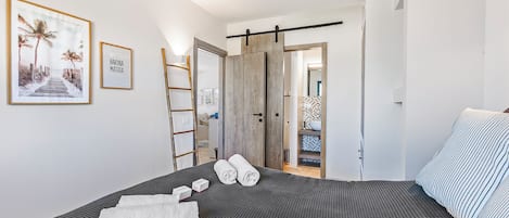 Una cama bien hecha con una revista, toallas y un cuadro en la pared.