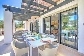 An outdoor dining area with a table set for a meal, surrounded by chairs, and a pergola overhead.