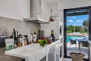 A modern kitchen with a large island, a built-in oven, and a view of a swimming pool. - Villa Tartaruga Luxury With Pool (Carovigno)