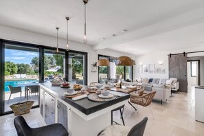 A modern kitchen with a large island, dining area, and a view of a swimming pool. - Villa Tartaruga Luxury With Pool (Carovigno)