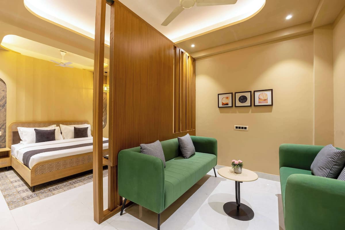 Ein modernes Hotelzimmer mit einem grünen Sofa, einem kleinen runden Tisch mit einer Blume und einem Bett mit einem Holz-Kopfstück.