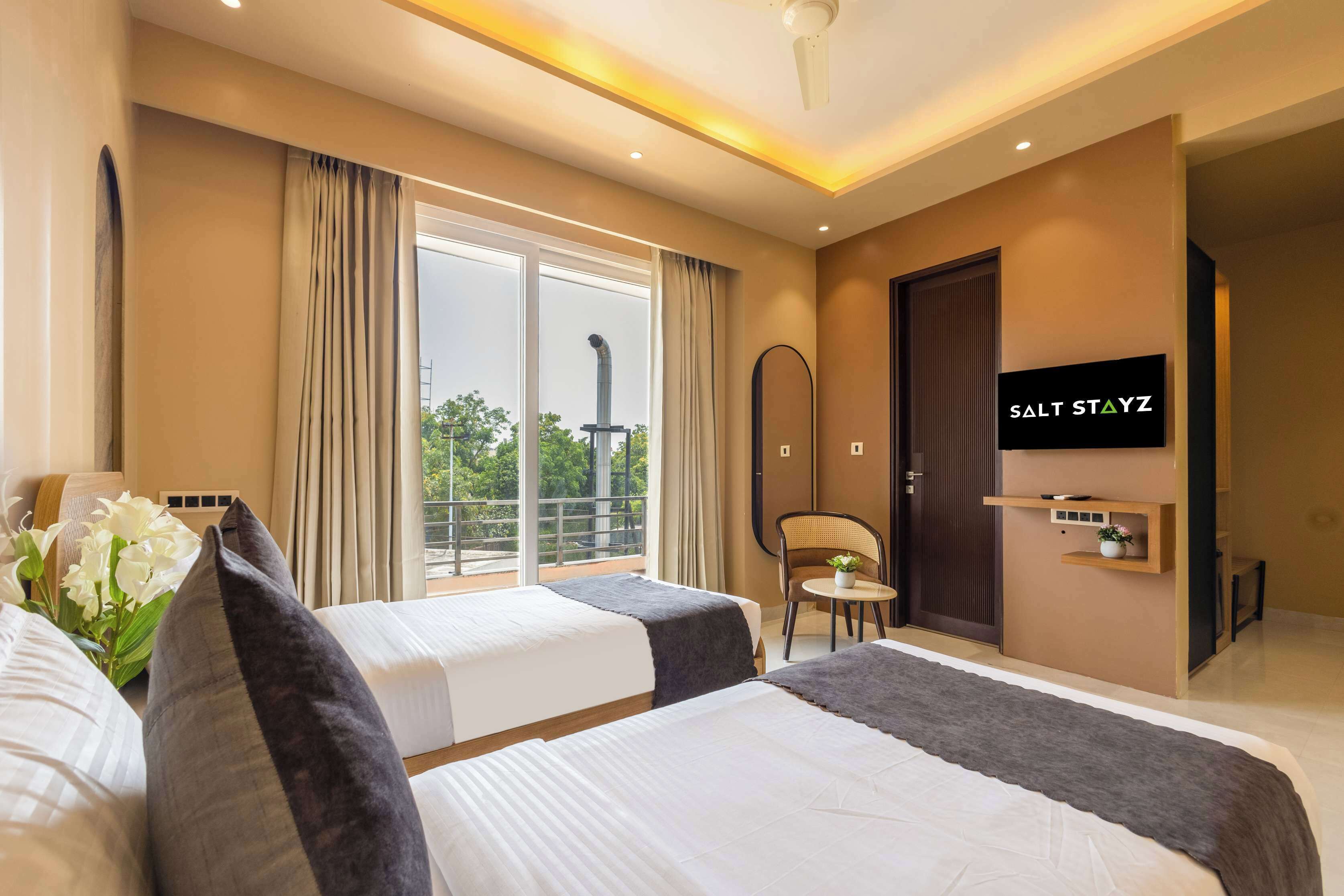 Habitación de hotel con dos camas, televisor, una mesita con una silla y balcón con cortinas.
