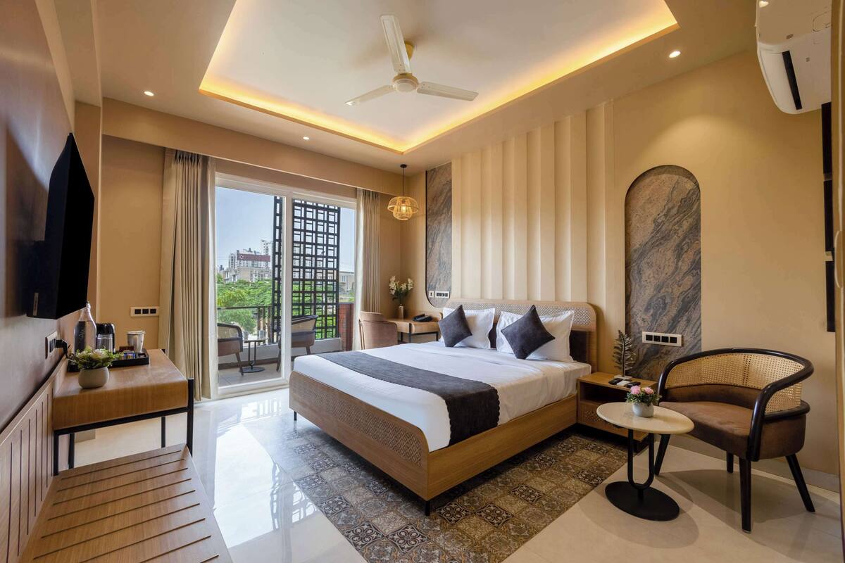 Ein modernes Hotelzimmer mit einem großen Bett, einem Schreibtisch, einem Sessel und einem Balkon mit Blick auf die Stadt.