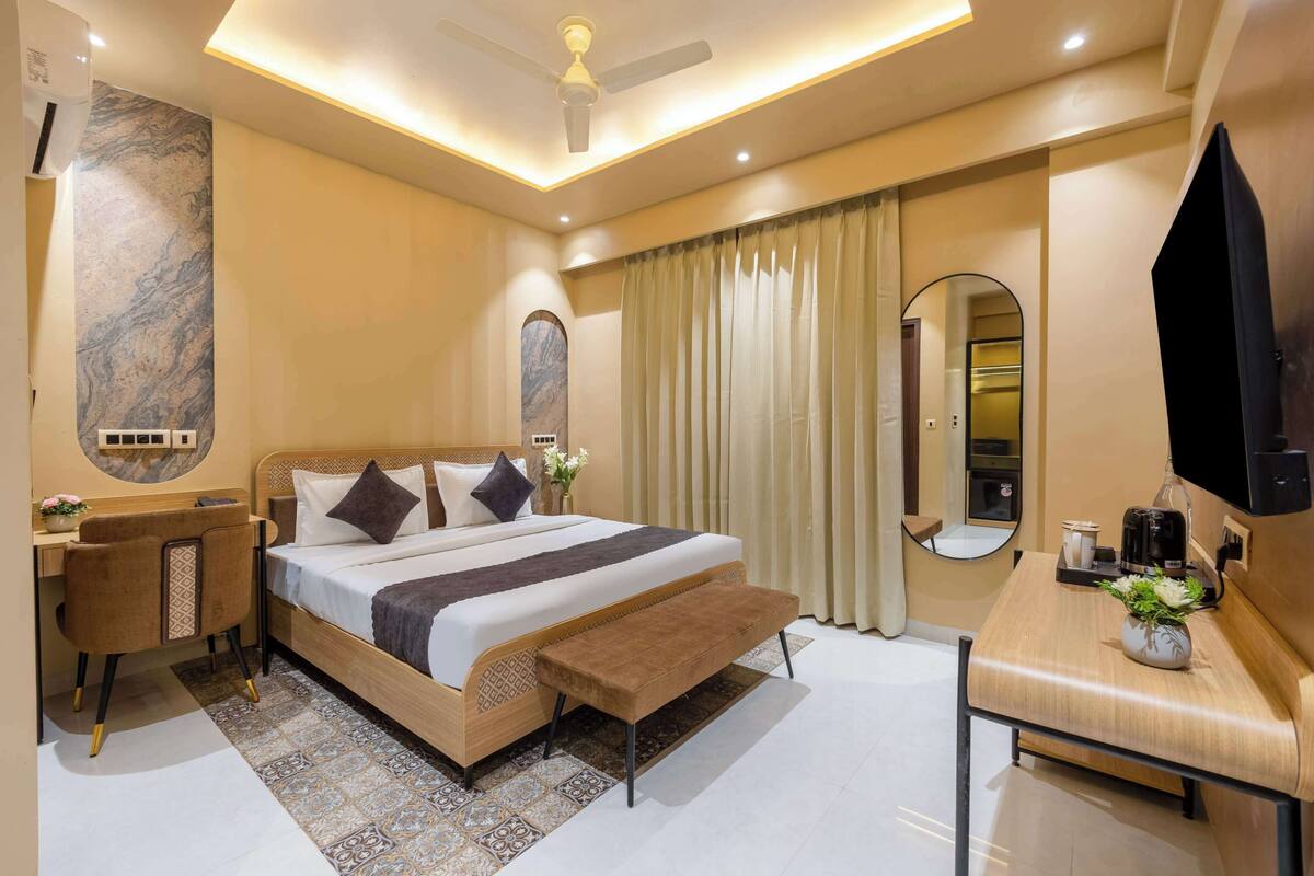 Ein modernes Hotelzimmer mit einem großen Bett, einem Schreibtisch, einem Sessel, einer Bank, einem Flachbildfernseher, einem Spiegel und einem Deckenventilator.