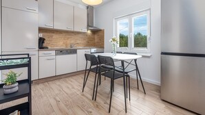 Una cocina moderna con armarios blancos, un refrigerador de acero inoxidable, un protector contra salpicaduras de madera y una zona de comedor con una mesa redonda y sillas.