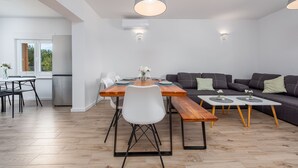 Una sala de estar moderna con comedor, que incluye una mesa de madera, sillas blancas, un sofá gris y una lámpara colgante gris.