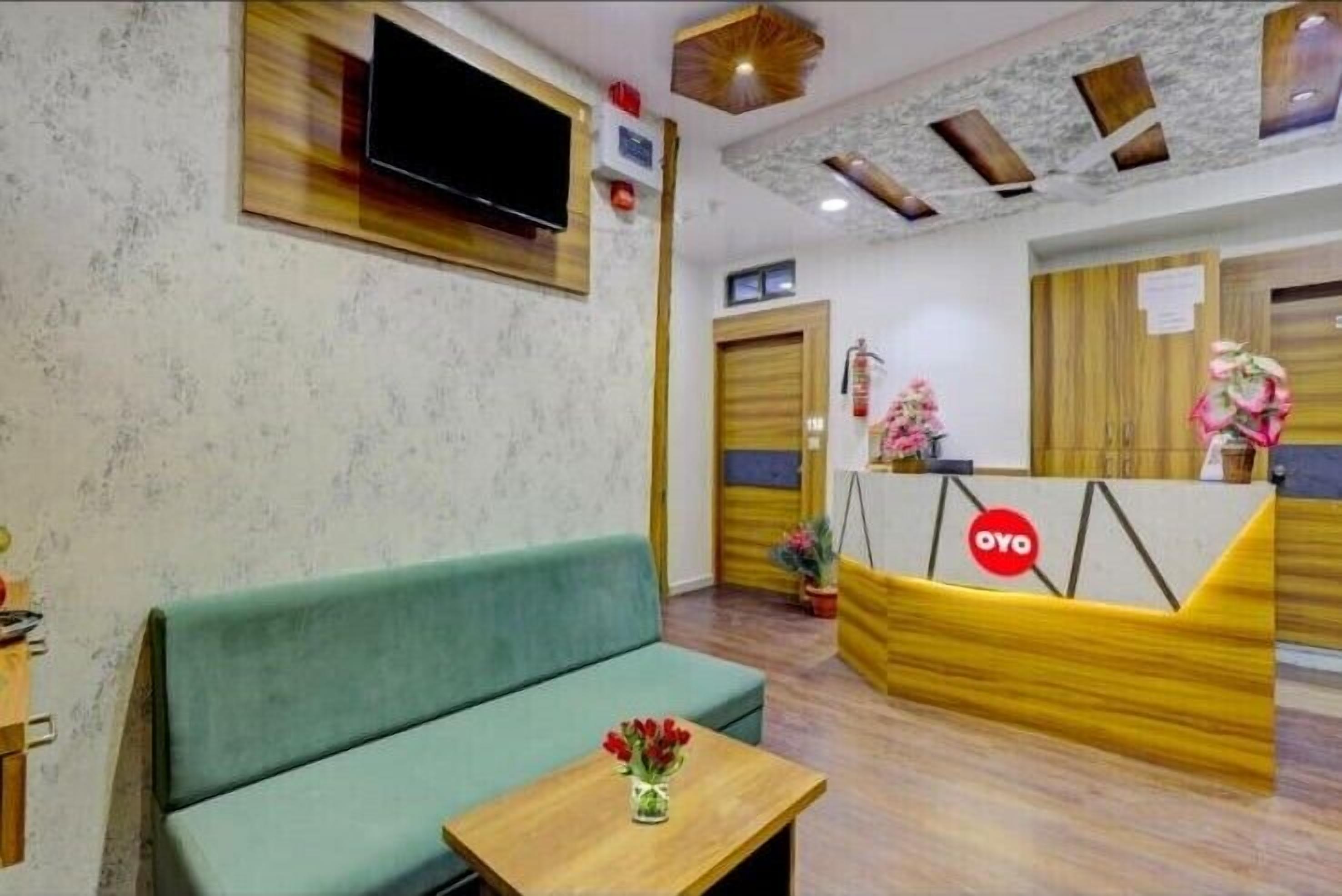 A reception area with a sofa, a small table with a vase of flowers, a reception desk, and a television mounted on the wall.