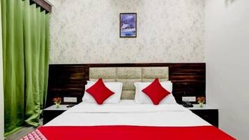 A hotel room with a bed, green curtains, a framed picture on the wall, and a red and white bedspread.