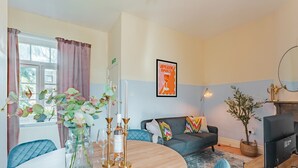 Ein Wohnzimmer mit einem runden Holztisch, einer Couch mit bunten Kissen, einem Fernseher und einem Kamin.