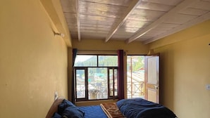 Une chambre avec deux lits, des poutres apparentes en bois au plafond, une fenêtre donnant sur la verdure et une porte menant à l’extérieur.
