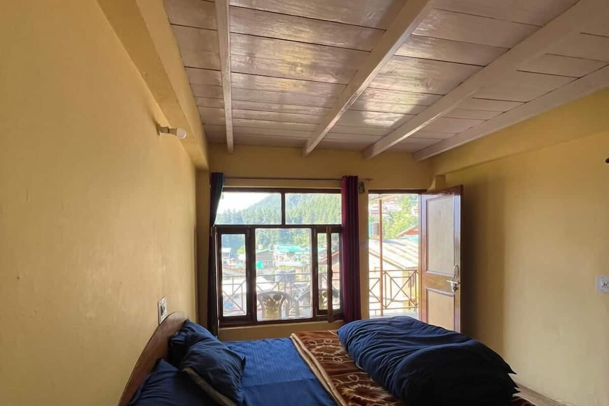 A room with two beds, wooden ceiling beams, a window with a view of greenery, and a door leading outside.