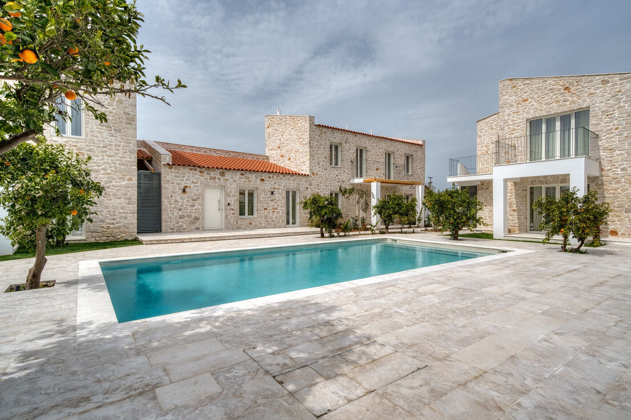A modern stone building with a swimming pool, surrounded by trees and a clear sky.
