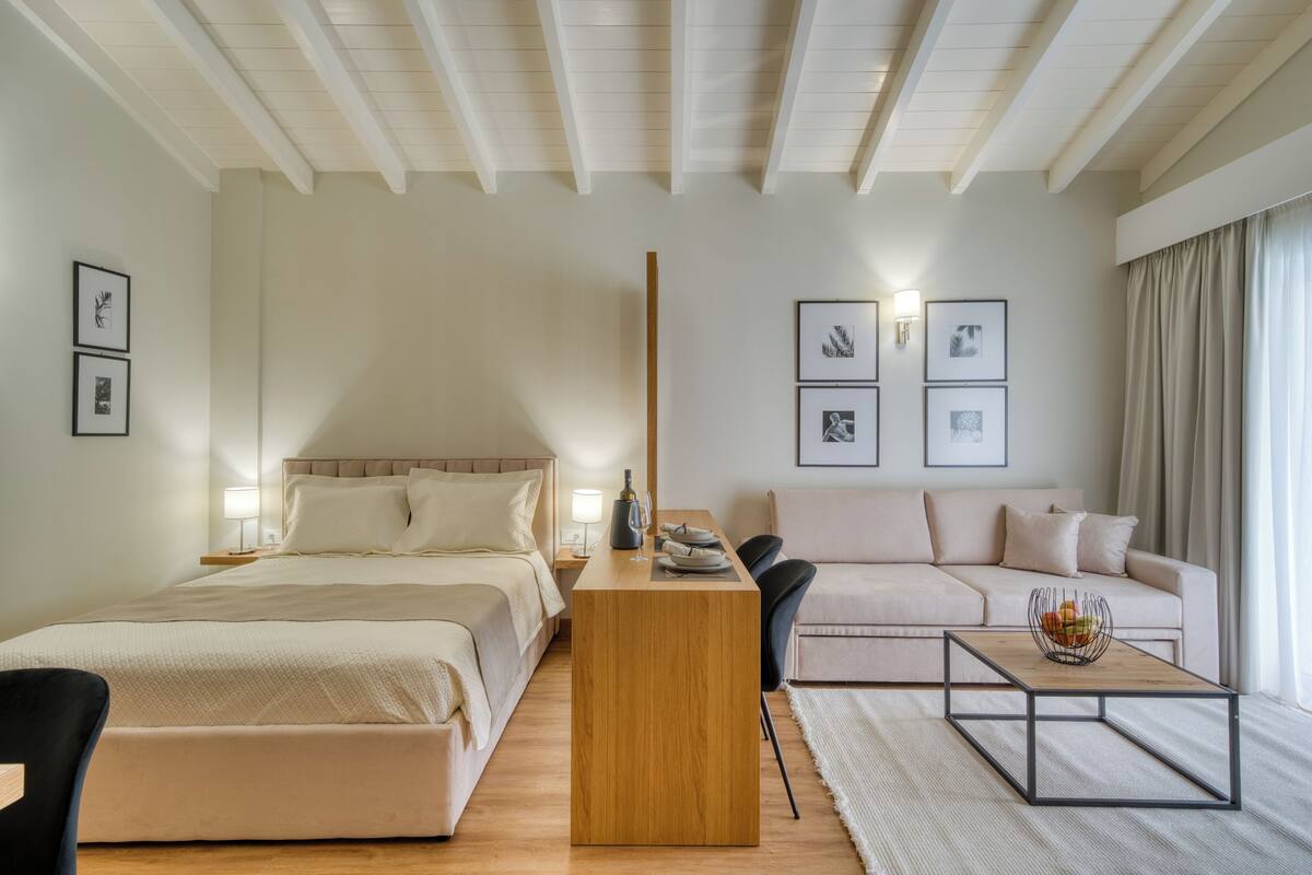 A hotel room with a bed, a wooden side table, a sofa, and a coffee table.