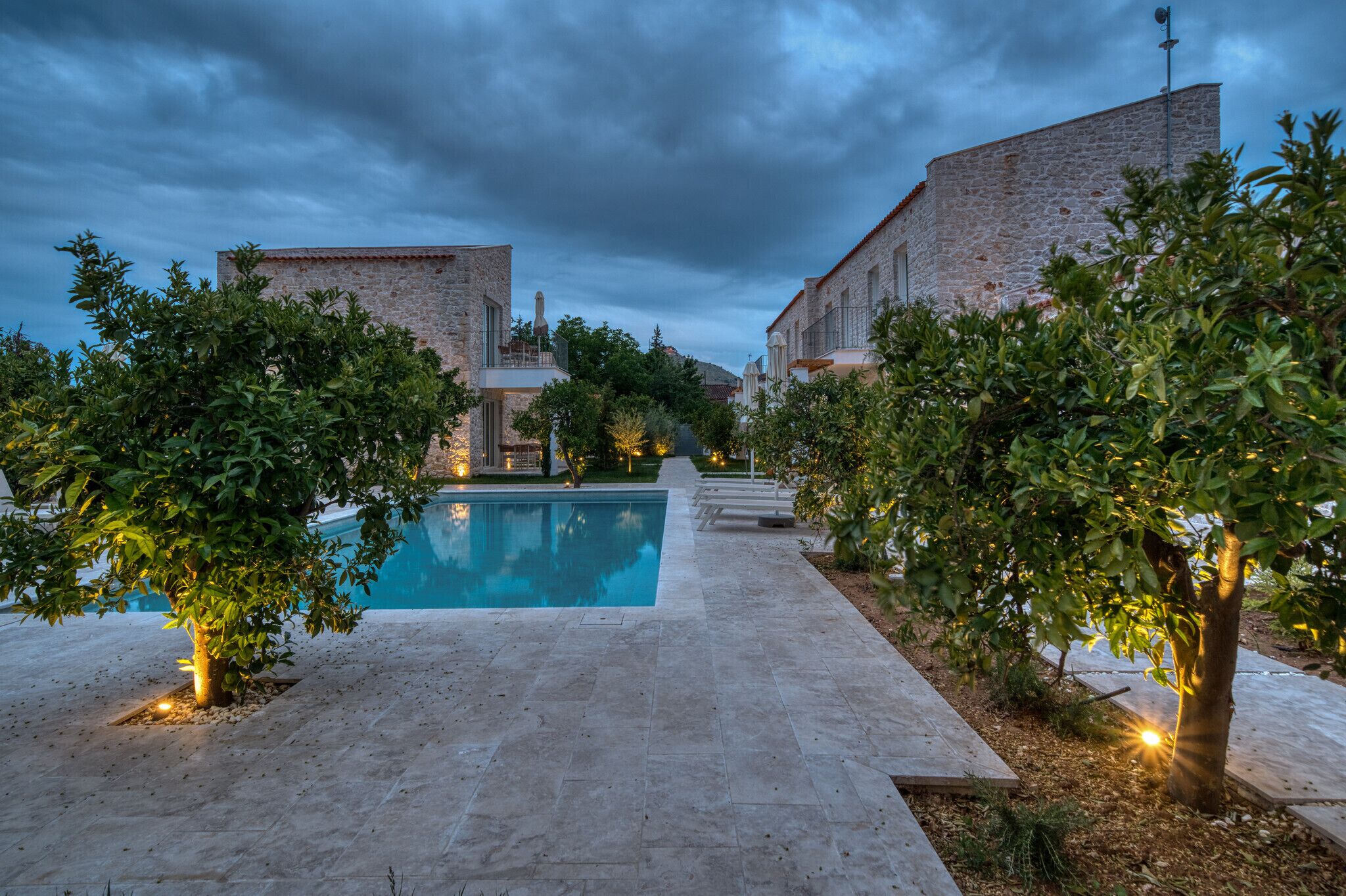 A courtyard with a swimming pool, stone buildings, and trees.