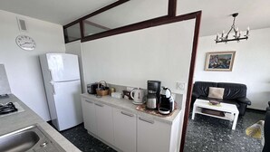 A compact kitchen with a refrigerator, toaster, coffee maker, and a small dining table.