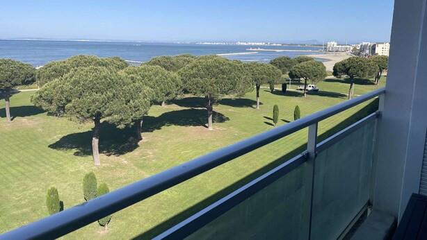 A balcony with a view of a grassy area with trees and a beach in the distance.