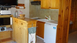 Une cuisine compacte avec des meubles en bois, un four à micro-ondes encastré, un lave-vaisselle et un téléviseur fixé au mur.