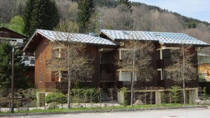 Une cabane en bois avec un toit en pente, entourée d’arbres et adossée à une montagne.