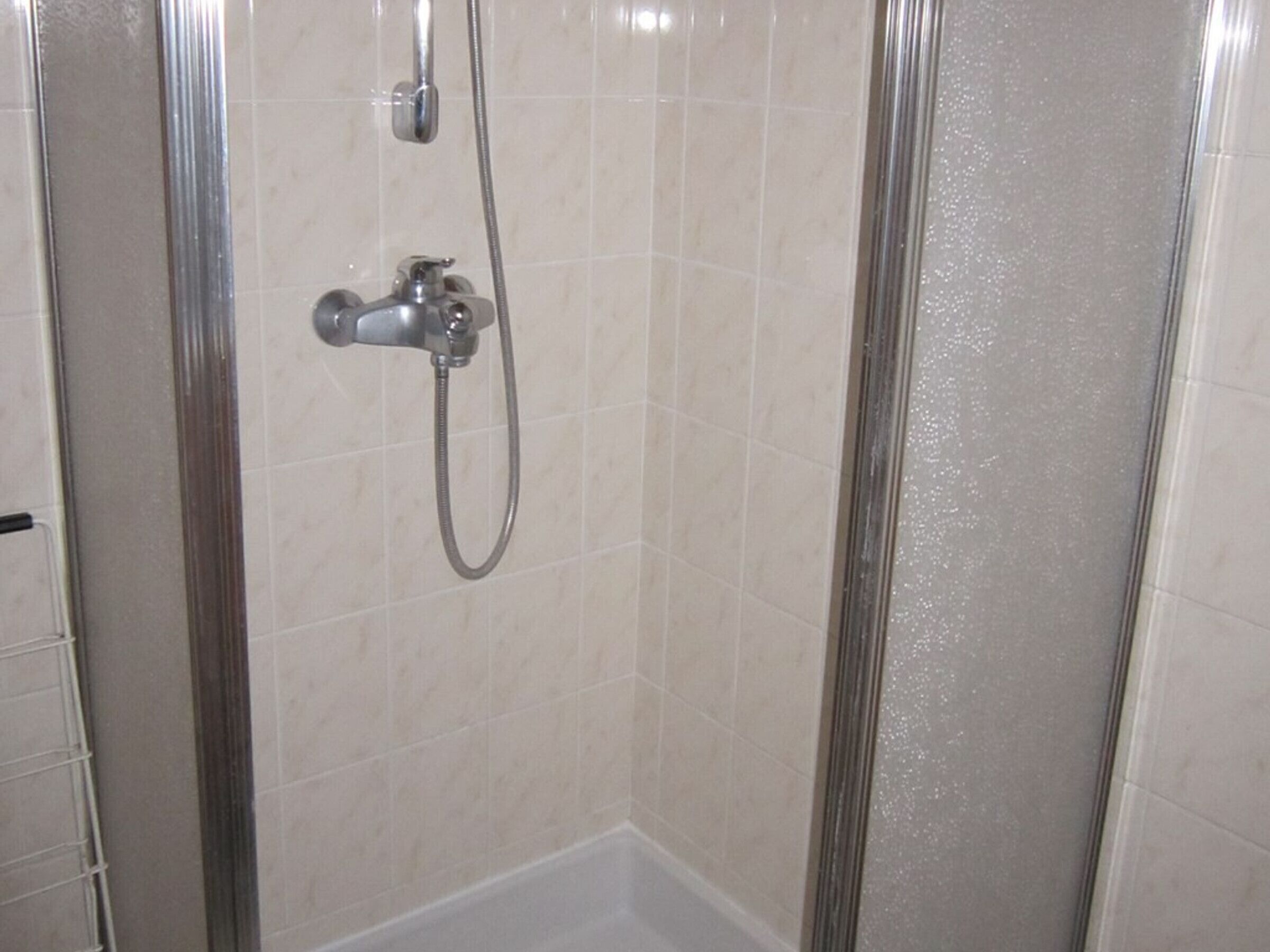 A shower enclosure with a handheld showerhead and a fixed showerhead.