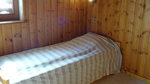 Un lit simple avec une couvre-lit à rayures, dans une pièce aux murs en bois et dotée d’une fenêtre.