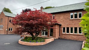 A brick building with a central tree with red leaves, surrounded by a flower bed. - Redstones Hotel (Appleby-in-Westmorland)