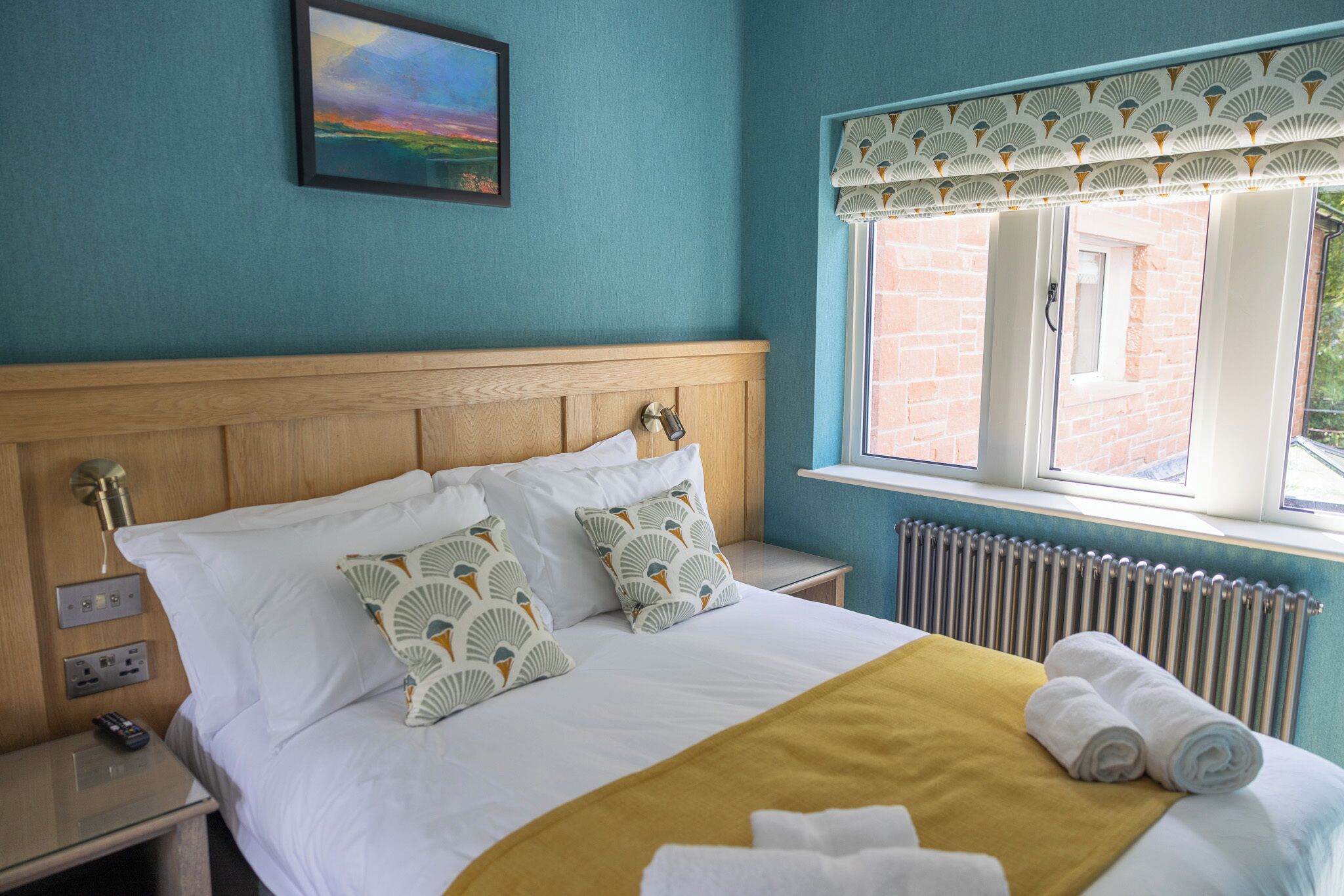Une chambre d’hôtel avec un lit, une table de chevet, une fenêtre donnant sur un beau paysage et un tableau au mur.