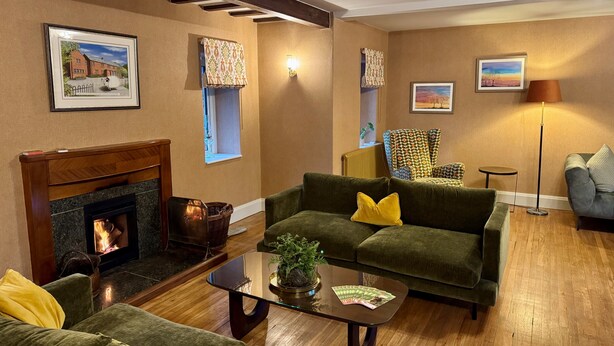 A cozy living room with a fireplace, green sofas, a coffee table, and a floor lamp. - Redstones Hotel (Appleby-in-Westmorland)