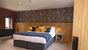 A bedroom with a large bed, a wooden headboard, a patterned wall, a nightstand, and a radiator. - Redstones Hotel (Appleby-in-Westmorland)