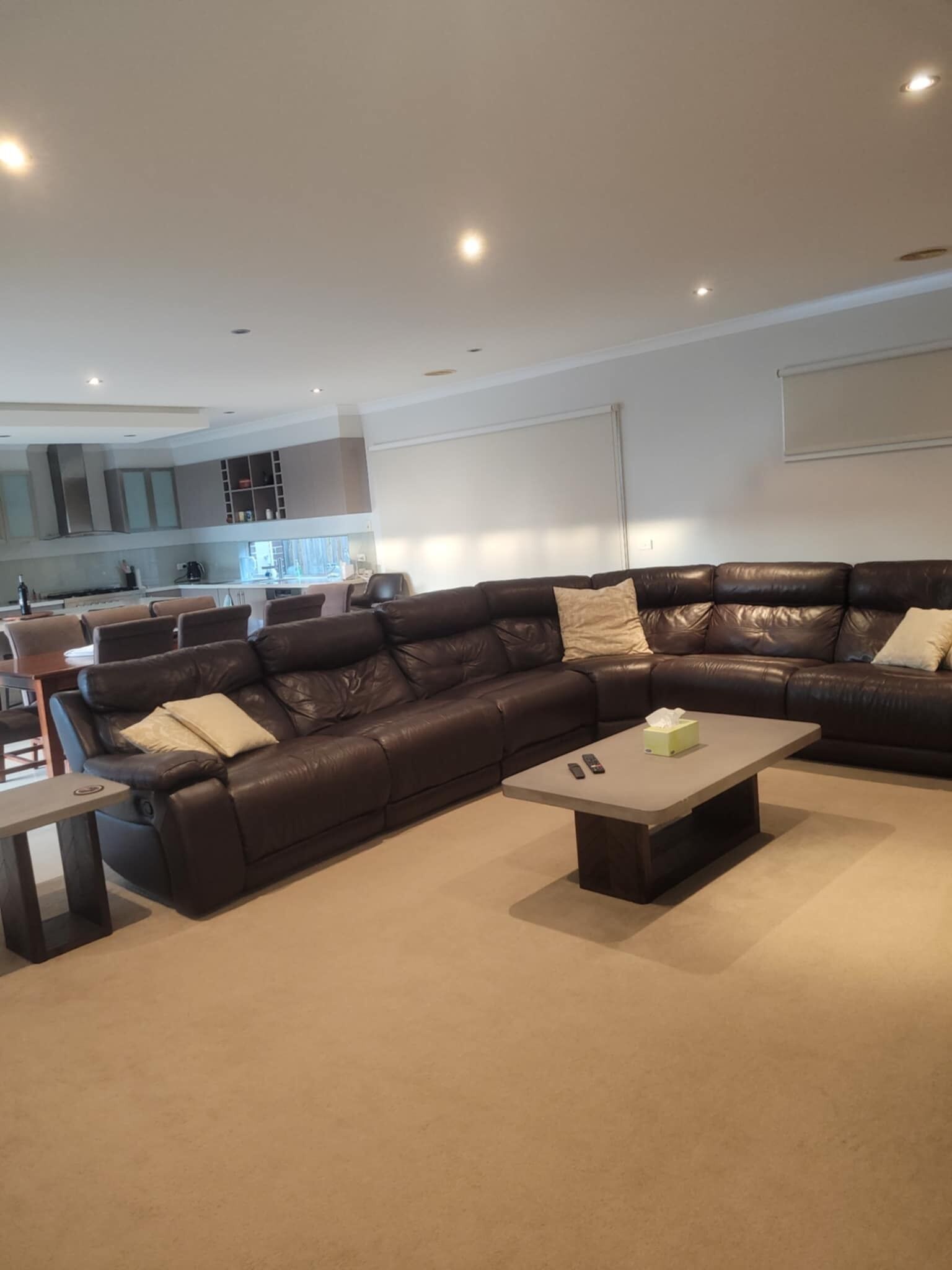 A modern living room with a dark leather sectional sofa, a small coffee table, and a kitchen in the background.