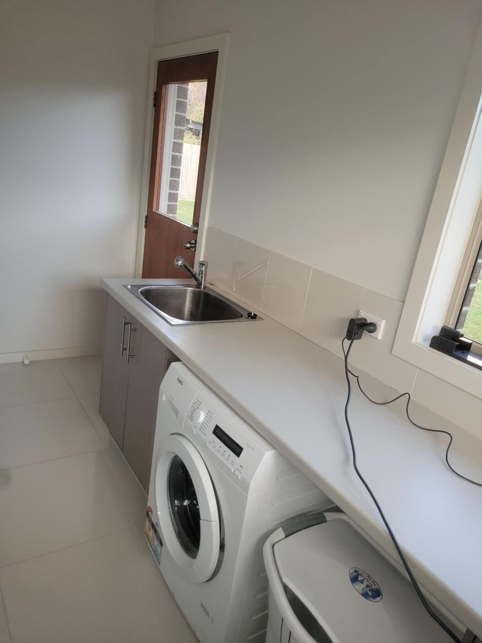 Une cuisine compacte équipée d’un lave-linge intégré, d’un évier et d’une fenêtre donnant sur l’extérieur.