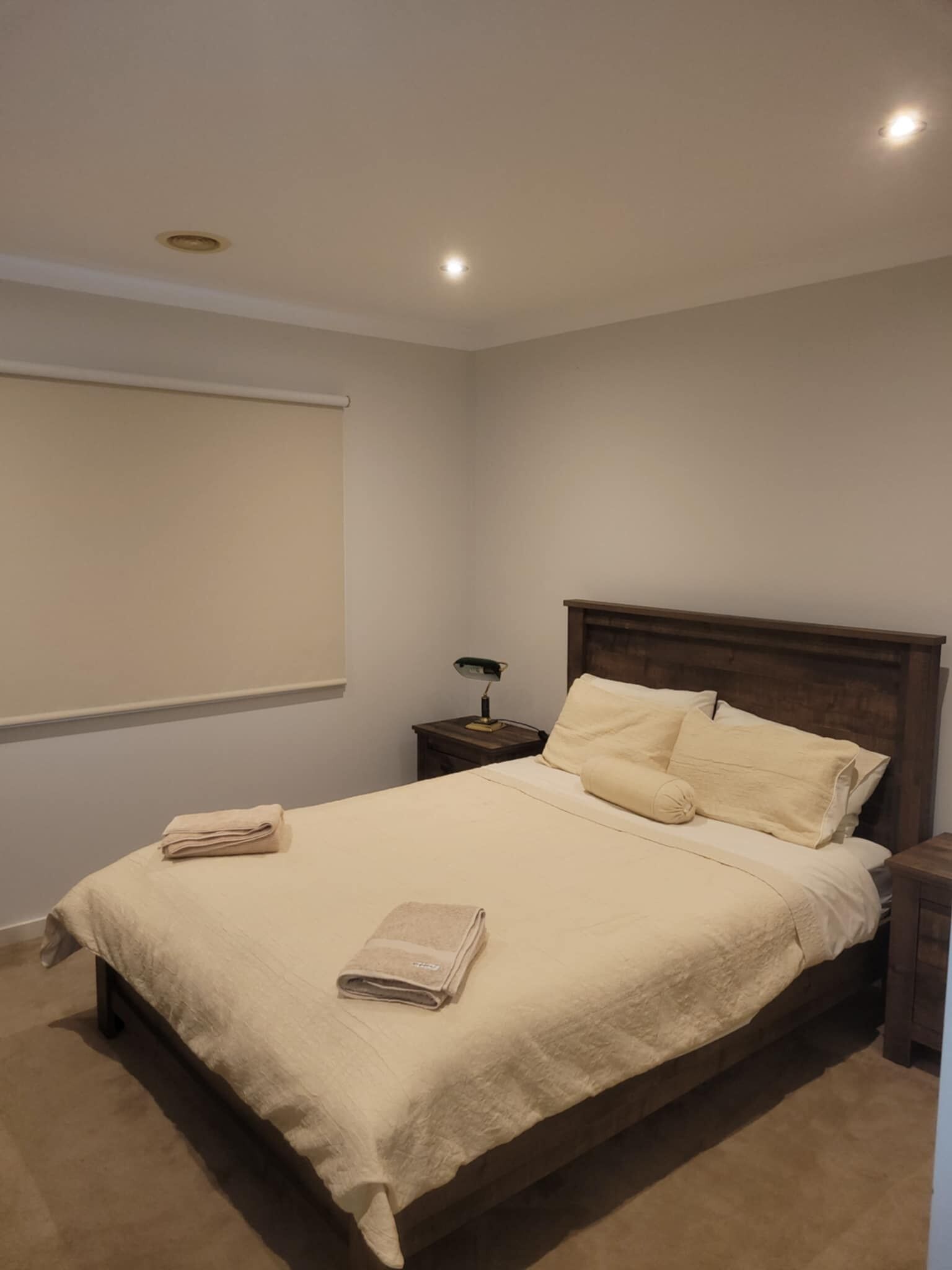 Un lit bien fait, avec une couette et des oreillers de couleur beige, une table de chevet avec une lampe et un luminaire au plafond.