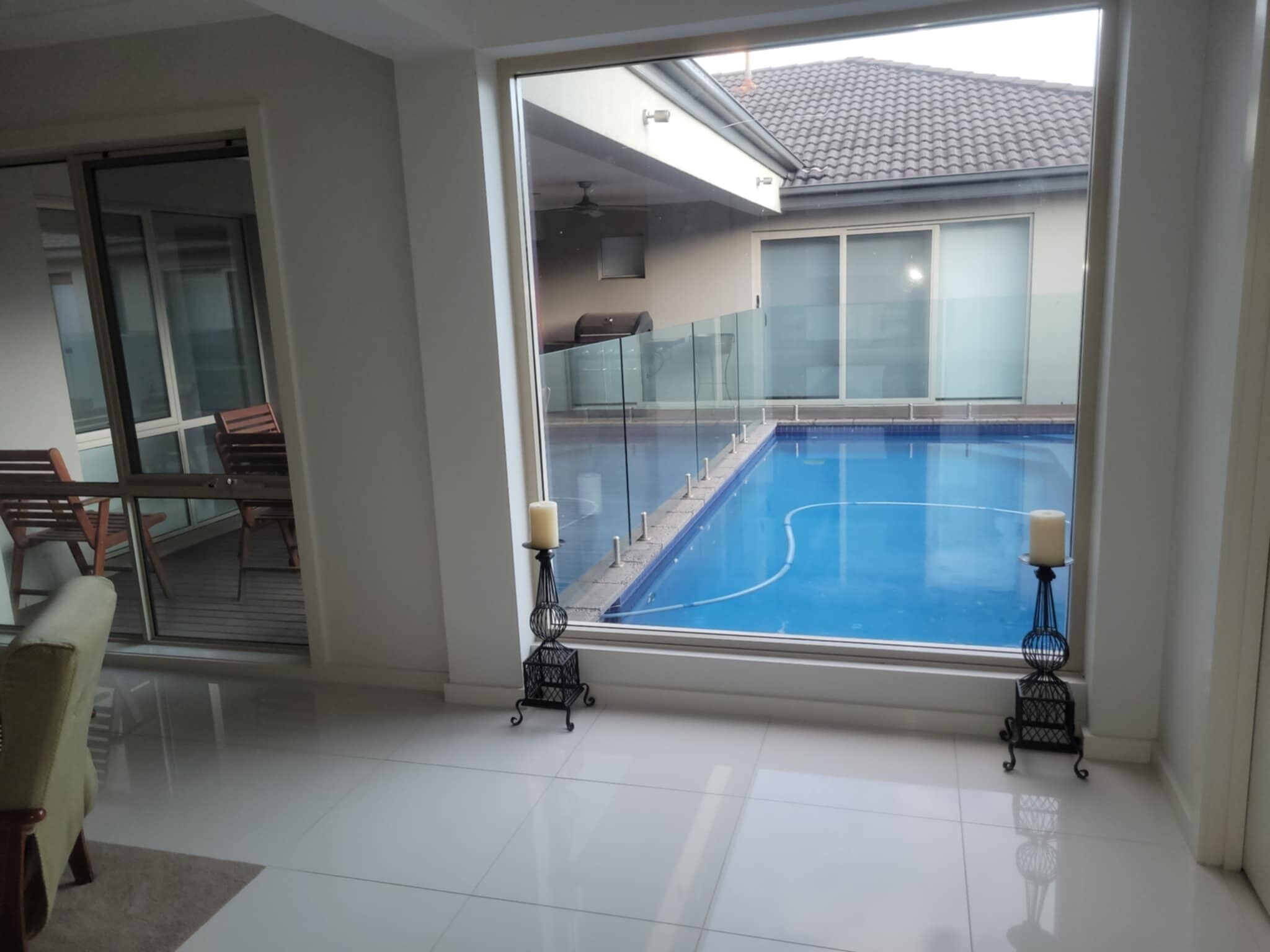 Un interior moderno con un amplio ventanal que da a una piscina, una puerta de cristal que conduce a un espacio exterior, y una zona de estar con sofá y sillones.