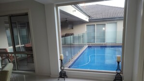 Een modern interieur met een groot raam met uitzicht op een zwembad, een glazen deur naar een terras en een zithoek met een bank en stoelen.