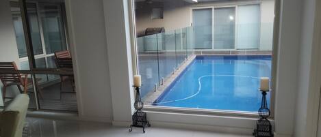 Un interior moderno con un amplio ventanal que da a una piscina, una puerta de cristal que conduce a un espacio exterior, y una zona de estar con sofá y sillones.