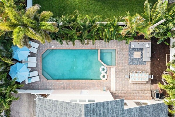 An aerial view of a swimming pool area with lounge chairs and umbrellas, surrounded by palm trees. - Steps 2 Beach | Pool/SPA | Game Room | Pool Table (Palm Beach Shores)