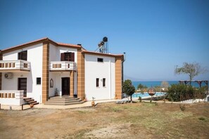 A two-story house with a swimming pool, a covered patio, and a view of the sea.