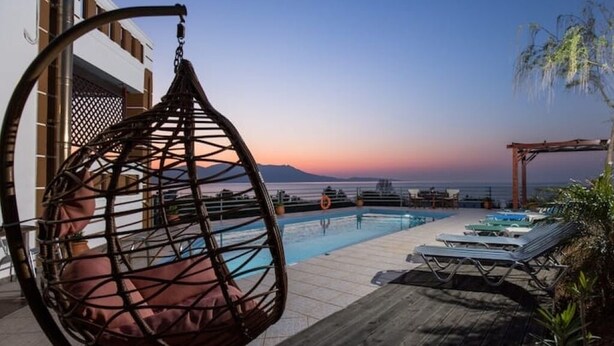 Ein Poolbereich mit Hängesessel, Liegestühlen und Blick auf das Meer bei Sonnenuntergang.