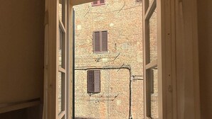 A room with a window opening to a brick building with shutters. - Pendulum - 9 (Siena)