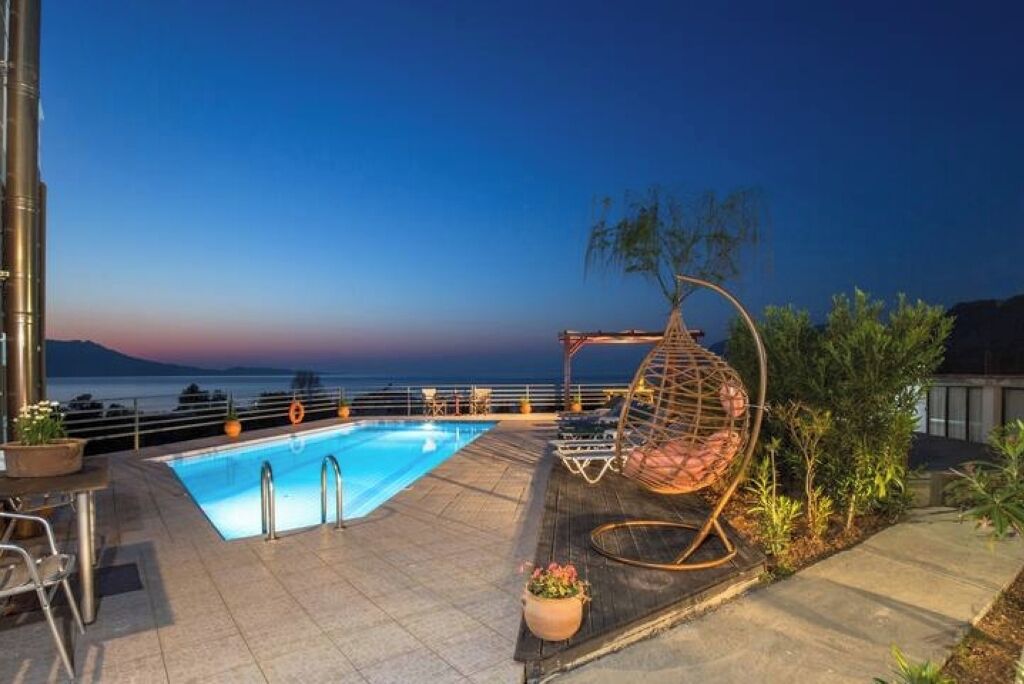 A pool area with a hanging chair, a table, and a view of the sea at dusk.