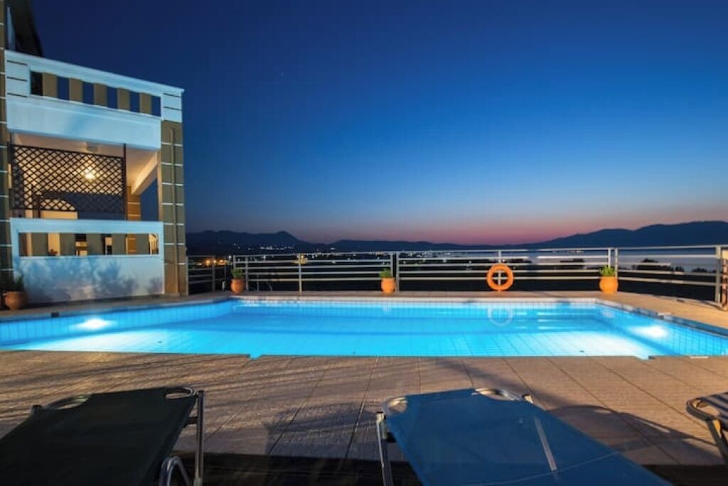 A swimming pool with lounge chairs, a building with a balcony, and a view of the horizon.